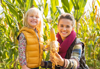Wall Mural - Happy mother and child showing corn while in cornfield