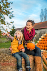 Wall Mural - Happy mother and child sitting on haystack with pumpkins and poi
