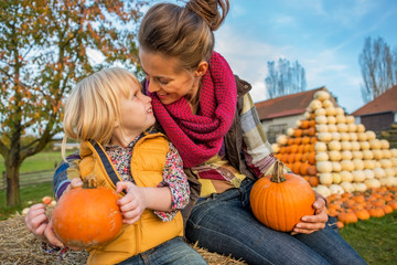 Wall Mural - Smiling mother and child sitting on haystack with pumpkins
