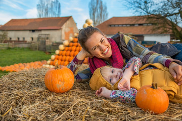 Wall Mural - Smiling mother and child laying on haystack with pumpkins