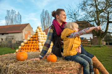 Wall Mural - Mother and child sitting on haystack with pumpkins and pointing