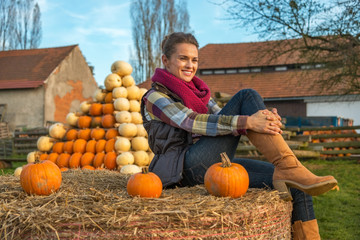Wall Mural - Portrait of young woman sitting on haystack with pumpkin