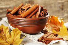 Cinnamon Sticks In Bowl With Yellow Leaves On Wooden Background