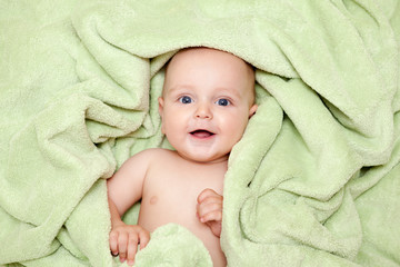 Caucasian baby boy covered with green towel joyfully smiles at c