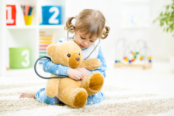 cute little girl playing doctor with plush toy at home