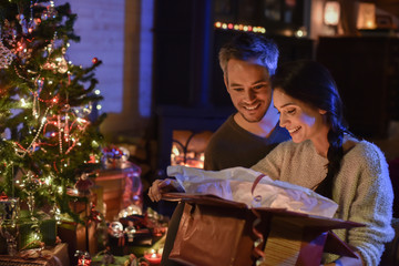 Wall Mural - Handsome couple opening a gift in front of the Christmas tree li