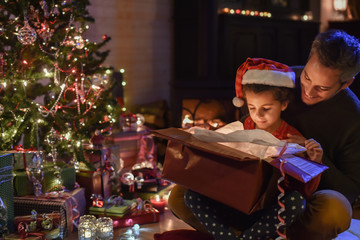 Wall Mural - Lovely little girl with a santa claus hat and her father opening