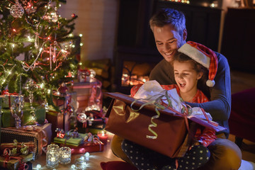 Wall Mural - Lovely little girl with a santa claus hat and her father opening