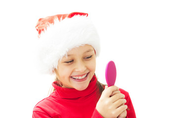 Wall Mural - Funny little girl in a Santa Claus hat looking in the mirror and