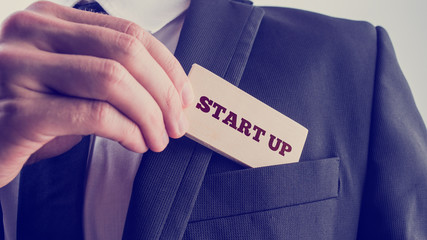 Businessman removing a wooden card reading Start up from his poc