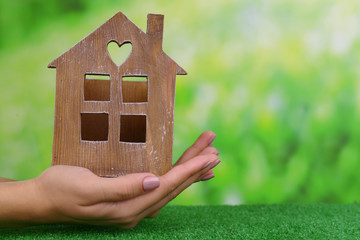 Sticker - Woman hands holding small house on grass on bright background