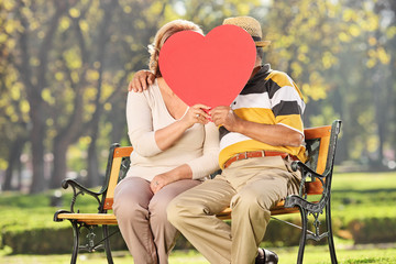 Poster - Mature couple kissing behind a red heart in a park