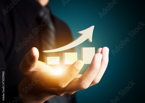 Fotografie, Obraz Hand holding a rising arrow, representing business growth.