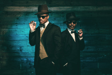 Two vintage african american gangsters smoking cigarette in fron