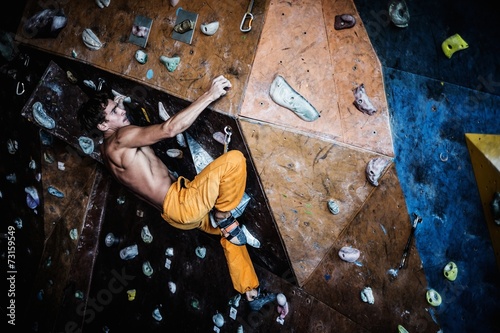 Cuadros en Lienzo Muscular man practicing rock-climbing on a rock wall indoors