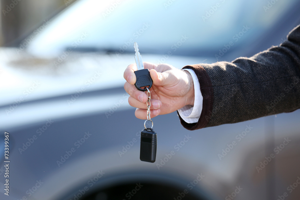 Male hand with car key on car background