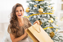 Happy Young Woman Opening Shopping Bag Near Christmas Tree