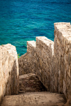 Ancient Stone Wall With Stairs Leading To Blue Sea