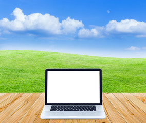 Laptop computer on wooden floor with green fields and blue sky b