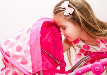 Cute smiling little girl playing with her toy carriage and doll