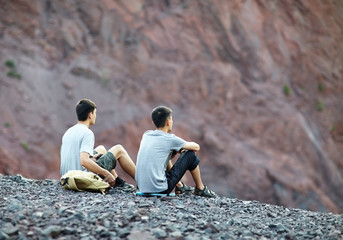 Wall Mural - Two young men sitting on rocky cliff