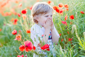 Cute kid boy with poppy flower on poppy field on warm summer day