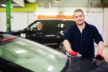 Wall Mural - Cheerful worker wiping car on a car wash