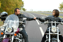 Two Bikers On Motorcycles Handshaking With Knuckle On Road