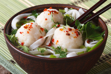 Wall Mural - Asian soup with fish balls, fresh herbs and rice noodles closeup