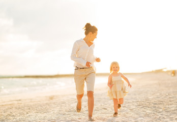 Wall Mural - Happy mother and baby girl running on beach at the evening