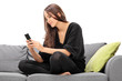 © Ljupco Smokovski - Young woman playing on her cell phone seated on a sofa