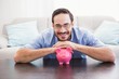© WavebreakMediaMicro - Smiling man laying on the piggy bank