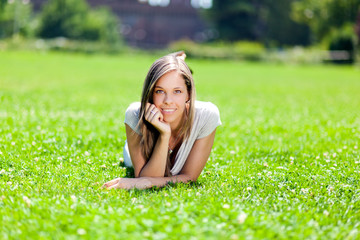 Wall Mural - Young smiling woman lying down on the grass