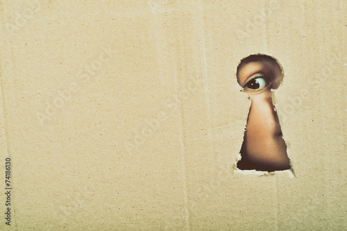 Fotografía Eye looking through a conceptual keyhole on cardboard, close up