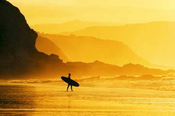 Wall Mural - surfer entering water at misty sunset