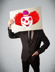 Wall Mural - Businessman holding a cardboard with a clown on it in front of h