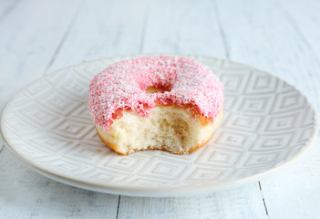 Bitten delicious donut on plate on wooden table close-up