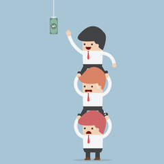 Business people carrying each other to reach hanging money