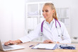 © lenets_tan - Beautiful young smiling female doctor sitting at the desk and
