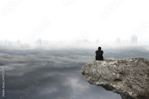Cuadros en Lienzo man sitting on cliff with gray cloudy sky cityscape background