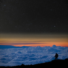 Wall Mural - lone climber above the clouds, looks at the starry night sky.
