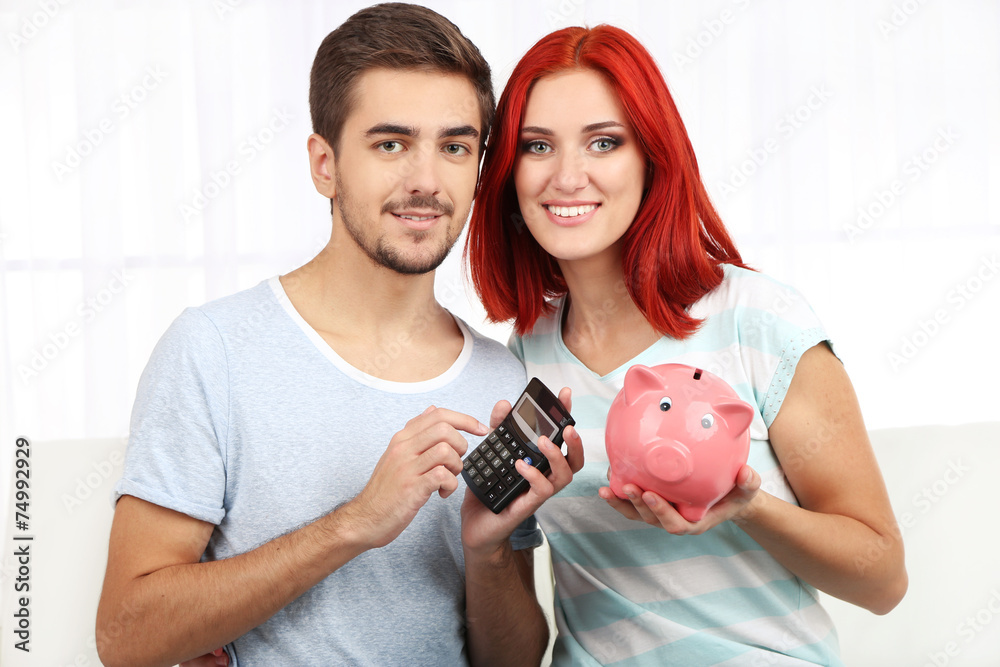 Loving couple sitting in sofa with piggy bank in room Stock Photo ...