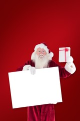 Poster - Composite image of santa shows a present while holding sign