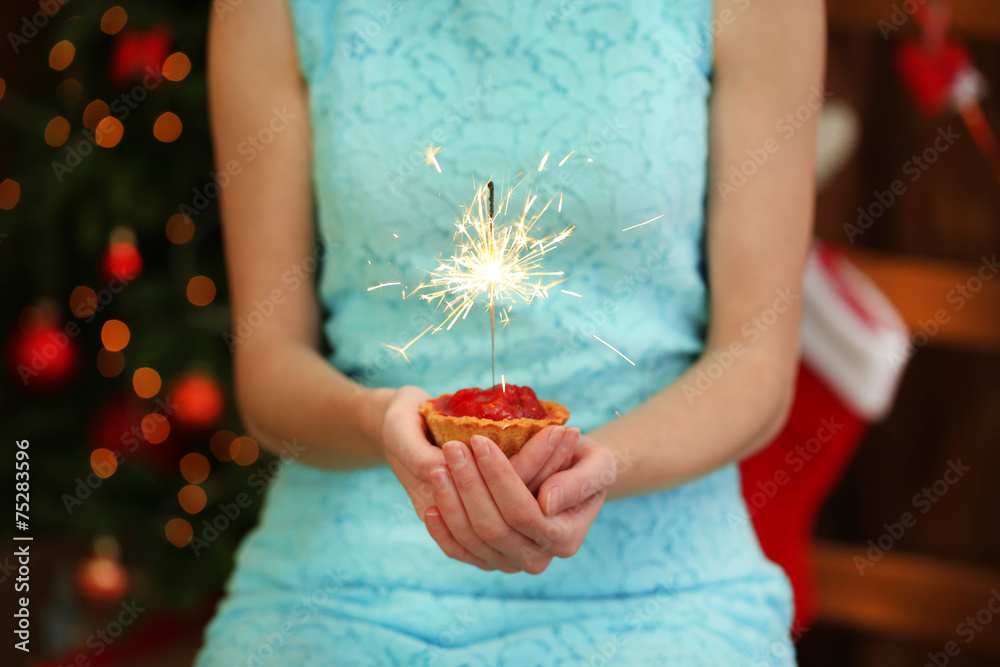Woman holding cake with sparkler, on shiny background