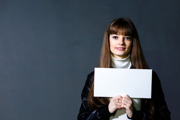 Young women holding empty white blank card on a dark wall backgr