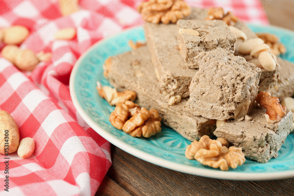 Sunflower halva with nuts on plate, on wooden background
