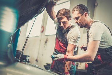 Two mechanics checking oil level in a car workshop