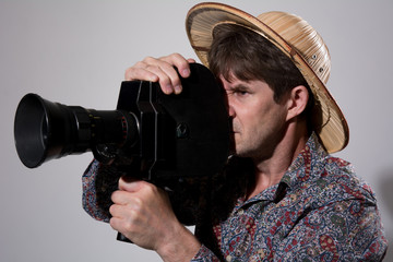 A man in a straw hat with an old movie camera on a gray backgrou