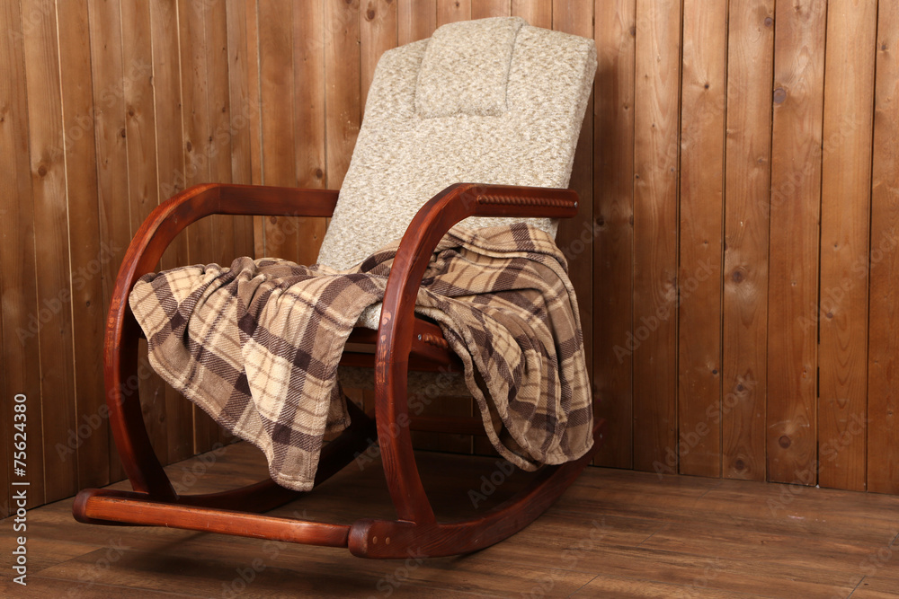 Rocking chair covered with plaid on wooden wall background