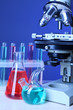 © Africa Studio - Microscope and test tubes on table, on color background
